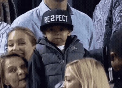 A Boy Wearing A Hat That Says Respect Is Sitting In A Crowd Of People . GIF