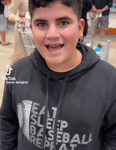 A Boy Wearing A Hoodie That Says Eat Sleep Baseball Repeat GIF