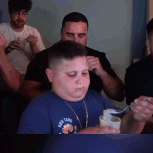 A Boy Wearing A Shirt That Says Aqui Tacos Is Eating Something With A Spoon GIF