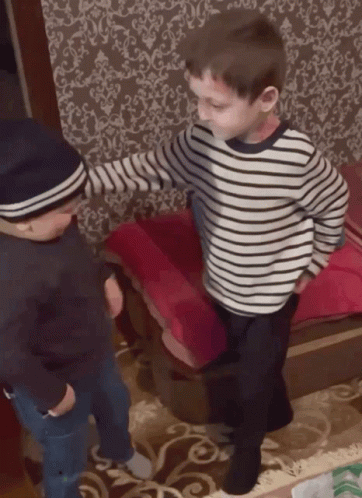 A Boy Wearing A Striped Shirt Is Standing Next To Another Boy Wearing A Hat GIF