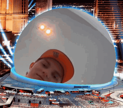 A Boy Wearing An Orange M & M 'S Hat Is Looking Out Of A Giant Dome GIF