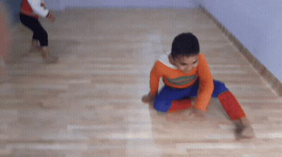 A Boy Wearing An Orange Shirt That Says ' Spiderman ' On It Is Doing A Handstand On The Floor GIF