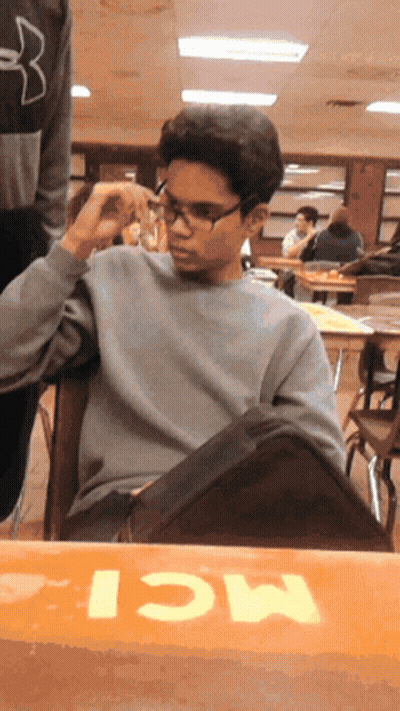 A Boy Wearing Glasses Sits At A Table With The Word Mci Written On It GIF