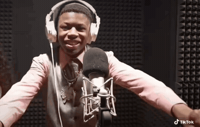 A Boy Wearing Headphones And A Pink Shirt Is Standing In Front Of A Microphone . GIF