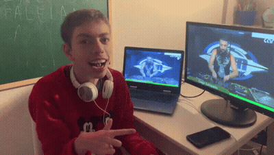 A Boy Wearing Headphones Is Sitting At A Desk In Front Of Two Monitors One Of Which Shows A Dj On It GIF