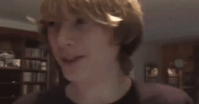 A Boy With Blonde Hair Is Smiling In A Dark Room GIF