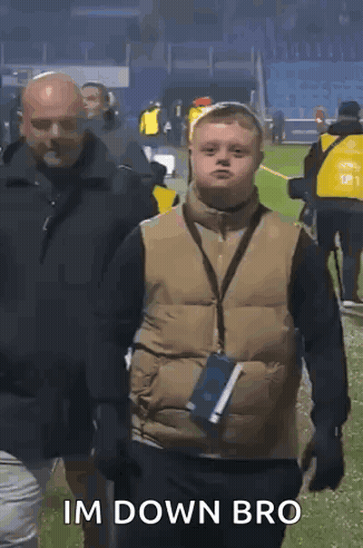 A Boy With Down Syndrome Is Walking On A Field With A Man Behind Him And Says Im Down Bro . GIF