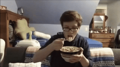 A Boy With Glasses Is Eating Cereal In A Bedroom GIF