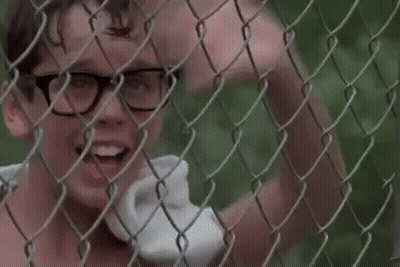 A Boy With Glasses Is Standing Behind A Chain Link Fence . GIF