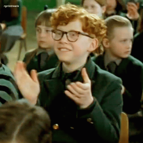 A Boy With Red Hair And Glasses Is Sitting In A Classroom With Other Children . GIF