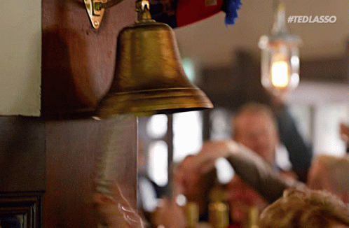 A Brass Bell Is Hanging On A Wooden Wall With The Hashtag #Tedlasso On It GIF