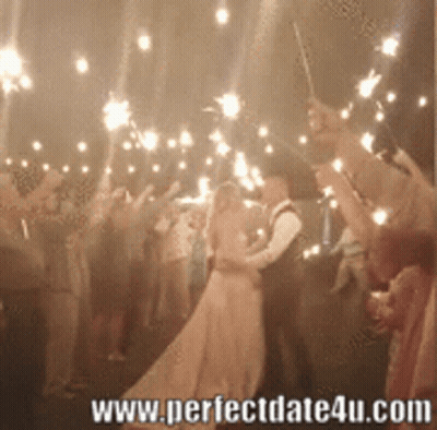 A Bride And Groom Are Kissing Under Sparklers At A Wedding GIF