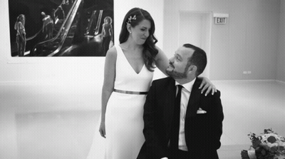 A Bride And Groom Are Posing For A Picture In Front Of An Exit Sign . GIF