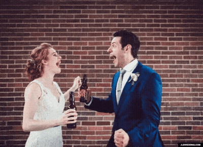 A Bride And Groom Are Toasting With Beer Bottles In Front Of A Brick Wall GIF