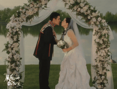 A Bride And Groom Kiss Under A Floral Arch With The Words Mother Gino 'S On The Bottom GIF