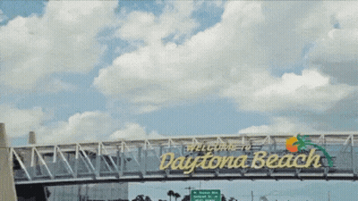 A Bridge Over A Highway With A Sign That Says Daytona Beach GIF