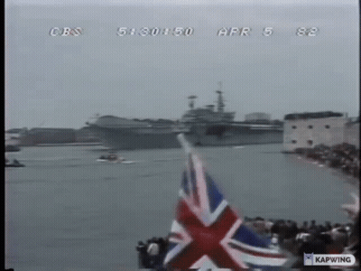 A British Flag Is Flying In Front Of A Large Ship On The Water GIF