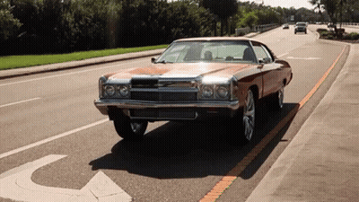 A Brown Car Is Driving Down A Street With A Handicap Sign On The Sidewalk GIF
