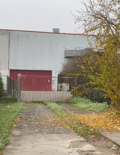 A Building With A Red Garage Door Is Behind A Gate GIF