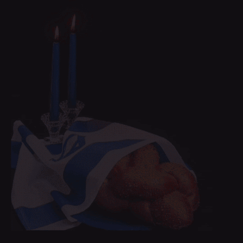 A Bunch Of Bread Is Wrapped In A Blue And White Cloth Next To Two Lit Candles GIF
