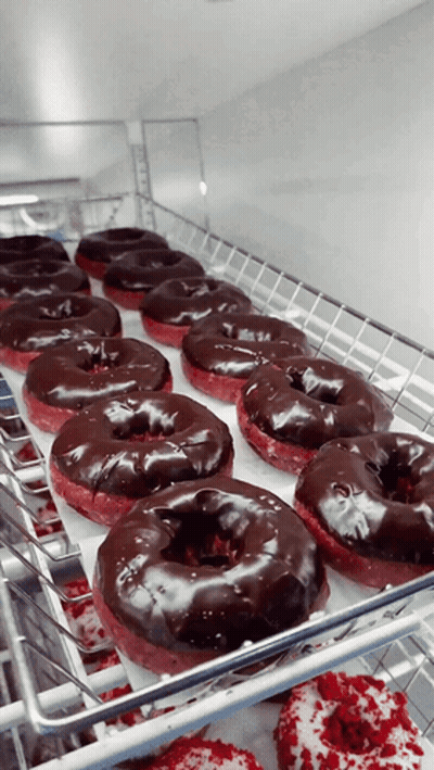 A Bunch Of Chocolate Covered Donuts Are Sitting On A Shelf GIF