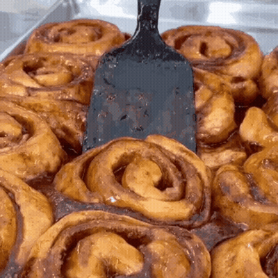A Bunch Of Cinnamon Rolls With A Spatula In The Middle GIF