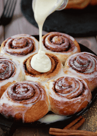 A Bunch Of Cinnamon Rolls With Frosting Being Poured On Them GIF
