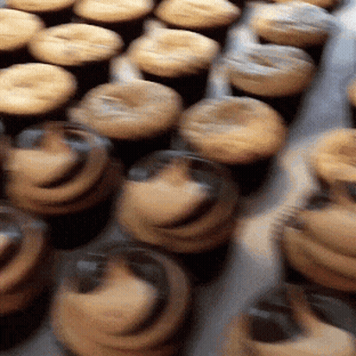 A Bunch Of Cupcakes With Frosting On Them Are Lined Up On A Table GIF