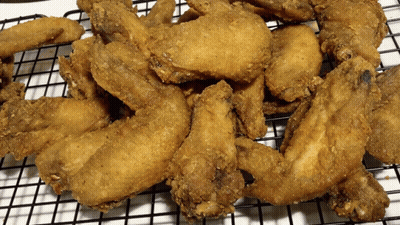 A Bunch Of Fried Chicken Wings Are Sitting On A Wire Rack GIF