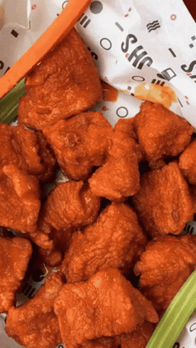 A Bunch Of Fried Chicken Wings With Celery And Carrots On A Paper That Says Shc GIF