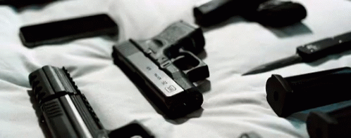 A Bunch Of Guns Are Laying On Top Of A Bed . GIF