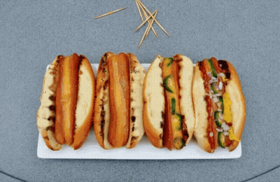 A Bunch Of Hot Dogs On A Plate With Toothpicks In The Background GIF