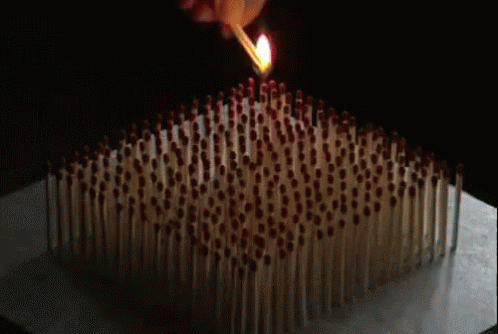 A Bunch Of Matches Are Sitting On Top Of Each Other On A Table And One Of Them Is On Fire . GIF