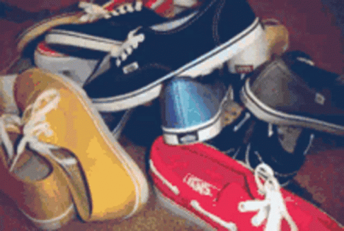 A Bunch Of Shoes Are Stacked On Top Of Each Other And One Of Them Has The Word Vans On It GIF