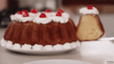 A Bundt Cake With Whipped Cream And Cherries On Top Of It GIF
