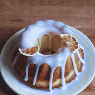 A Bundt Cake With White Frosting And Slices Of Orange On A White Plate GIF
