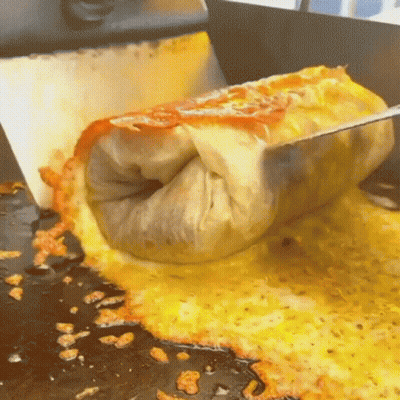 A Burrito Is Being Cut In Half On A Stove Top GIF