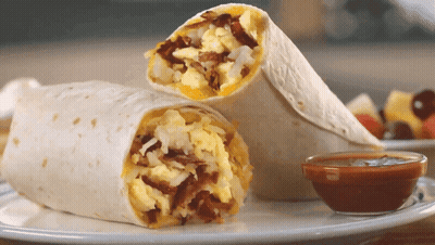 A Burrito Is Cut In Half On A Plate Next To A Bowl Of Sauce GIF