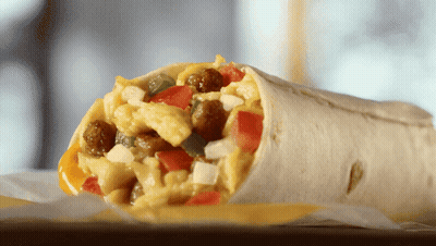 A Burrito With Scrambled Eggs Sausage Tomatoes And Cheese On A Table GIF