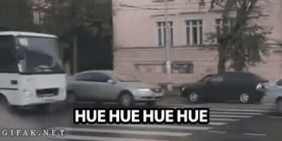 A Bus Is Driving Down A City Street Next To A Car And A Building . GIF
