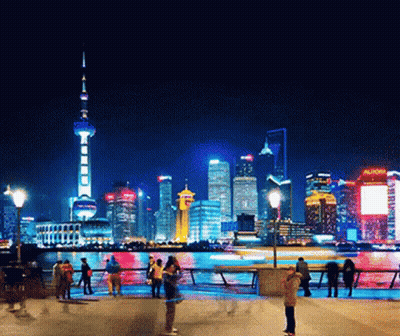 A Busy City At Night With A Sign That Says Aunow GIF