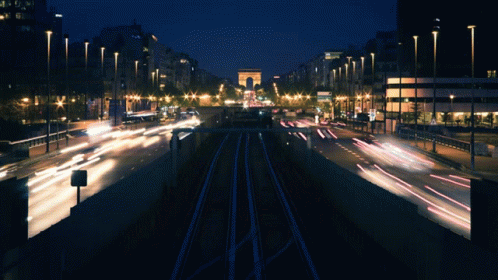 A Busy City Street At Night With A Large Archway In The Background GIF