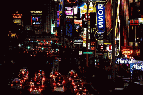 A Busy City Street At Night With A Mcdonald 'S Sign In The Foreground GIF