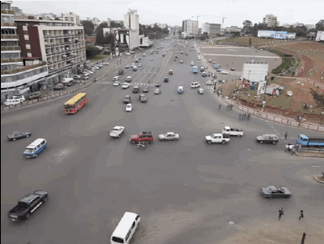 A Busy Intersection With Lots Of Cars And Trucks And A Billboard That Says ' Coca-Cola ' On It GIF