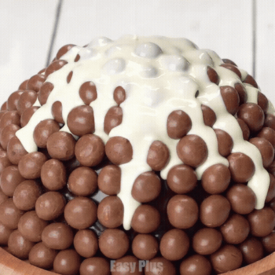 A Cake Covered In Chocolate Balls And White Frosting With Easy Plus On The Bottom GIF