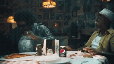 A Can Of Pepsi Sits On A Table With Two Men Eating Pizza GIF