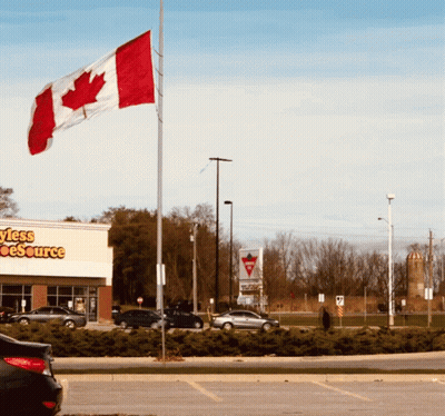 A Canadian Flag Is Flying In Front Of A Store Called Styles Source GIF