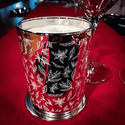 A Candle In A Silver Cup With Leaves On It Is On A Red Table GIF