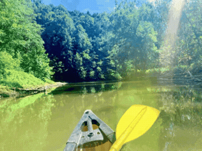 A Canoe With A Yellow Paddle Is Floating Down A River GIF