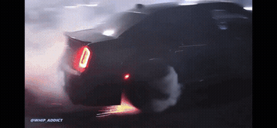 A Car Is Doing A Burnout In The Dark With Smoke Coming Out Of The Tire GIF